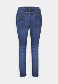 Jeans ajustados en denim azul oscuro, con una cintura de altura media, bolsillos traseros y un ligero desvanecimiento en las piernas. Detalles de costura en amarillo.