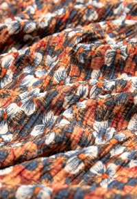 Gros plan sur un tissu texturé avec des motifs floraux orange, bleu marine et blancs, présentant des plis et des froissements visibles.