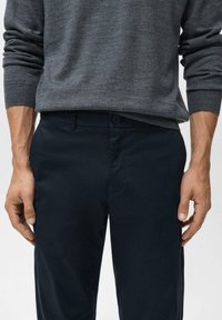 Mörkblå, skräddarsydda byxor med en slät yta, med knäppning fram och fickor, kombinerade med en grå, lätt tröja.