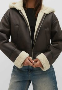 Veste en simili cuir marron avec un col et des poignets en shearling blanc. Dotée d'une fermeture éclair à l'avant et de poches latérales, avec un design ample.