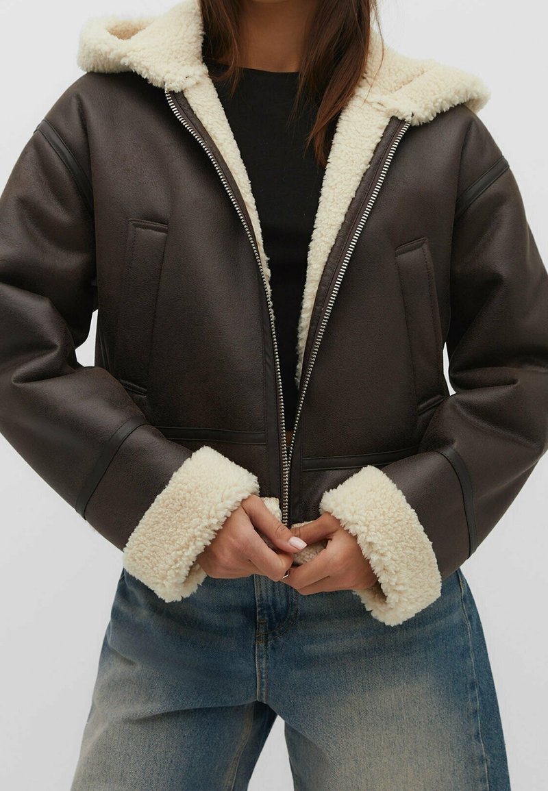 Veste en simili cuir marron avec un col et des poignets en shearling blanc. Dotée d'une fermeture éclair à l'avant et de poches latérales, avec un design ample.