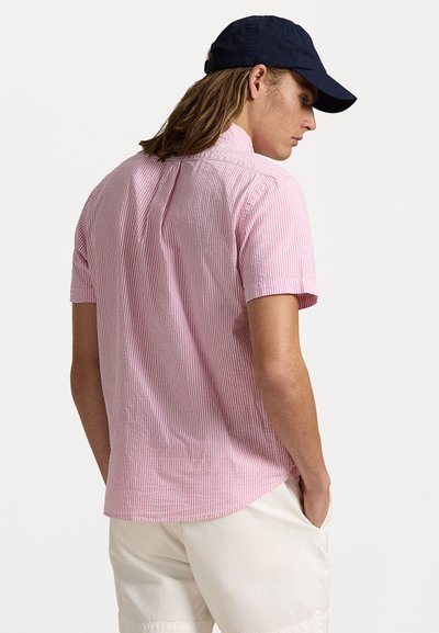 Košile s krátkým rukávem s pruhy v růžové a bílé barvě, s vrchní č�ástí na zádech, vyrobena z lehkého materiálu a s volným střihem. V kombinaci s námořnickou čepicí.