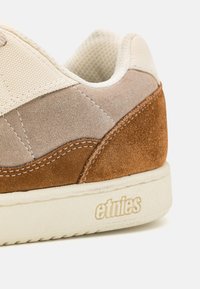 Beige ja ruskea mokkanahkainen lenkkari, jossa on teksturoitu verkko, kerma välikenkä ja kohotettu "etnies"-logo. Ominaisuuksiin kuuluu erottuva ompelu ja sileät pinnat.