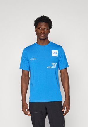Camiseta de algodón azul con cuello redondo, mangas cortas, que presenta un parche de logo y texto impreso en el frente en blanco. Corte relajado con textura suave.