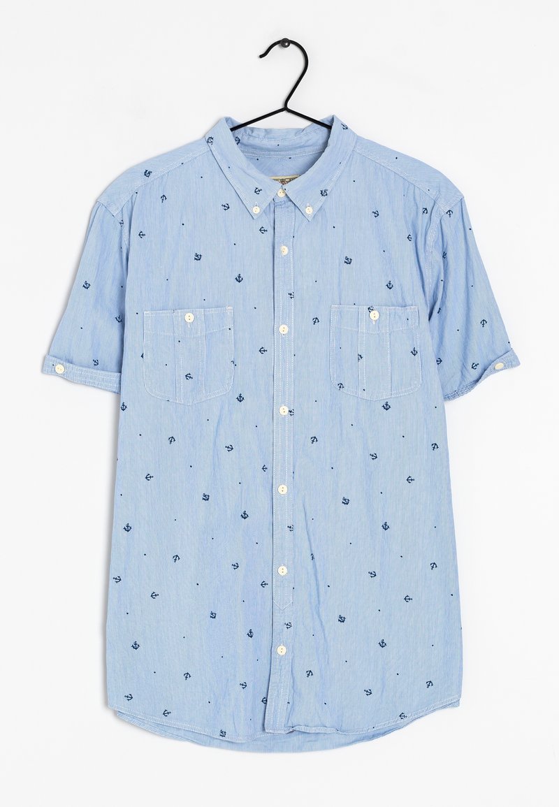 Chemise à manches courtes bleu clair avec petits motifs d'ancres bleu marine, deux poches poitrine et un col boutonné, suspendue sur un cintre noir.