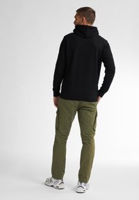 Felpa nera con cappuccio e vestibilità comoda, abbinata a pantaloni cargo verde oliva con tasche laterali. Sneakers bianche e nere completano il look.