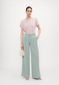 Top de rayas en rosa claro con mangas cortas, combinado con pantalones de pierna ancha en verde menta. La modelo sostiene un pequeño bolso color crema y lleva sandalias plateadas.
