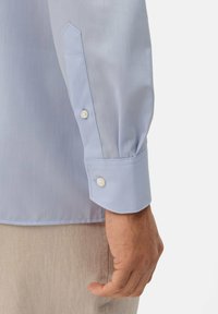 Lichtblauw overhemd met lange mouwen en puntige manchetten, voorzien van twee parelknopen. Glad stof met een lichte glans en een slim fit.