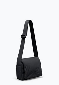 Sac messager noir avec une texture douce et rembourrée. Doté d'une longue sangle ajustable et d'une forme rectangulaire. Design minimaliste sans embellissements.