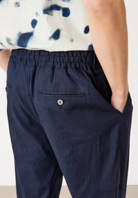 Marinblå byxor i lätt tyg med elastisk midja, sidofickor och en bakficka med knappdetalj.