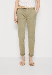 Khaki chinos se rovnými nohavicemi, ohrnutými manžetami a postranními kapsami. Doplněné pleteným béžovým opaskem a propletenými hnědými sandály.