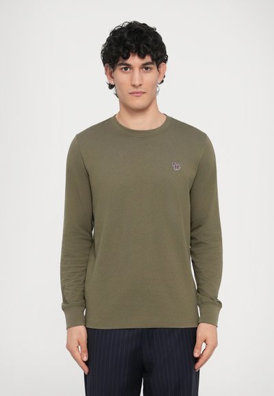 Πράσινο μακρυμάνικο μπλουζάκι από βαμβάκι με στρογγυλή λαιμόκοψη, που διαθέτει ένα μικρό πολύχρωμο λογότυπο στο αριστερό στήθος. Σχεδιασμός με ίσια γραμμή.