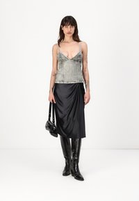 Gray denim tank top with thin straps, paired with a black draped satin skirt. Model wearing high black glossy boots and holding a small black handbag.