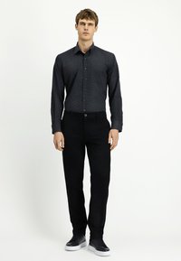 Ciemnoszara koszula na guziki z kieszonką, w połączeniu z czarnymi spodniami i czarnymi trampkami z białymi podeszwami. Gładki materiał o dopasowanym kroju.
