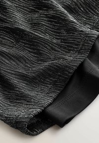 Mustast tekstuuriga kangas, millel on metallist hõbedased niidid ja laineline muster. Servas on must siledast materjalist serv, mis täiendavad disaini.