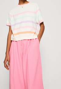 Top blanco de manga corta con rayas horizontales en tonos pastel de rosa, lavanda, azul y naranja. Combinado con pantalones anchos rosas.