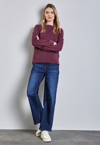 Felpa bordeaux con scollo rotondo, maniche lunghe, abbinata a jeans ampi blu scuro e sneakers bianche. Look semplice e casual.