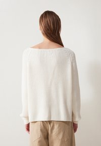 Krémový pletený svetr s volnějším střihem, širokým výstřihem a žebrovanou texturou. Rukávy jsou lehce zúžené u manžet.