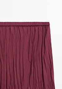 Jupe plissée bordeaux avec une taille élastique. Le tissu présente une apparence texturée et froissée. Design mi-long pour plus de polyvalence.