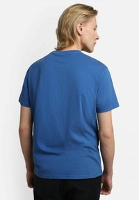 T-shirt in cotone blu con maniche corte, collo rotondo e una texture liscia, mostrata da dietro. Design minimale, senza loghi visibili.