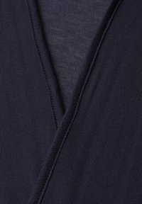 Mørk marineblåt strikket stof med en synlig V-formet søm, der fremhæver tekstur og stingdetaljer på tøjet.