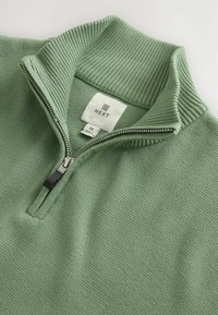 Lichtgroene gebreide pullover met een ribbelkraag en een halve rits, met het merklabel "NEXT" en maat "M" aan de binnenkant van de kraag.