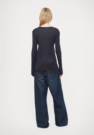 Top lung cu mâneci lungi de culoare bleumarin cu decolteu rotund, asociat cu blugi lejeri de denim ușor albastru, care au buzunare la spate și o siluetă relaxată.