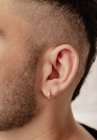 Pendiente de aro de oro en un cabello corto y muy rapado. El pendiente tiene una textura suave y forma circular, reflejando la luz de manera sutil.