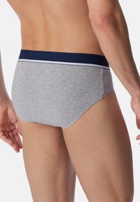 Graue Baumwollunterhosen mit einem marineblauen Bund, ausgestattet mit einer weißen Akzentlinie, eng anliegend und mit glatter Textur. Die Rückansicht hebt den Schnitt und die Passform hervor.