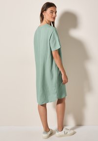 Mintgrünes Kleid mit kurzen Ärmeln, lockerer Passform, mittellanger Schnitt bis zur Oberschenkelmitte und abgerundetem Saum. Kombiniert mit weißen Sneakers mit hellgrünen Akzenten.