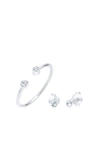 Set di gioielli in argento composto da un anello a bracciale con due pietre trasparenti e orecchini a perno coordinati, entrambi con superfici lucide e un design minimalista.