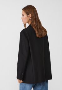 Schwarzer Blazer mit lässigem Schnitt, scharfen Revers, einer einzigen Knopfleiste und glatter Textur, kombiniert mit hellblauen Jeans.