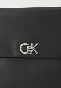 Black faux leather bag featuring a silver logo accent. The surface has a textured finish with a fold-over top closure.