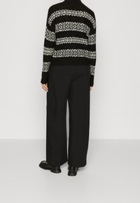 Zwart-wit gestreepte gebreide trui met lange mouwen, geribbelde manchetten en een ronde onderrand. Gekozen met brede zwarte broek en zwarte schoenen.