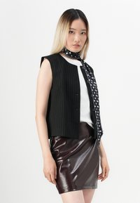 Gilet a righe nere indossato sopra una maglia bianca, abbinato a una mini gonna bordeaux lucida e a una sciarpa di seta nera a pois legata al collo.
