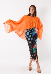 Cappa arancione trasparente con maniche fluide abbinata a un vestito nero aderente caratterizzato da vivaci motivi floreali e accenti.