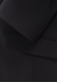 Gros plan sur un blazer noir montrant le revers qui se chevauche et une poche à rabat avec des coutures détaillées.