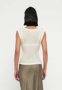 Ανοιχτό μπεζ αμάνικη μπλούζα με εφαρμοστή σχεδίαση, ριμπ υφή και στρογγυλή λαιμόκοψη. Η πίσω όψη δείχνει ελαφρά διαφάνεια και λεπτομέρειες ραφών.
