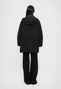 Zwarte hoodie met een losse pasvorm, voorzien van een trekkoorddetail op de rug. Het materiaal lijkt soepel, ontworpen met lange mouwen en een rechte snit.