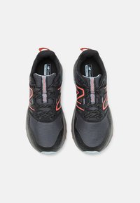 Zapatillas deportivas en negro y gris con parte superior de malla, acentos rojos y suela texturizada. Cuenta con un sistema de cordones y un cuello acolchado para mayor soporte.