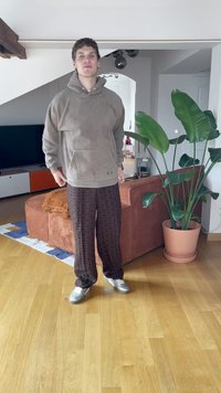 Felpa in pile marrone con tasca frontale e pantaloni scuri a fantasia con un design a diamante. Scarpe argento che riflettono la luce. Ambientazione interna.