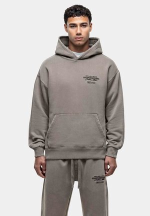 Hoodie gris surdimensionné avec une poche frontale, un capuchon à cordon de serrage et un texte imprimé. Tissu doux et poignets côtelés complètent le design.