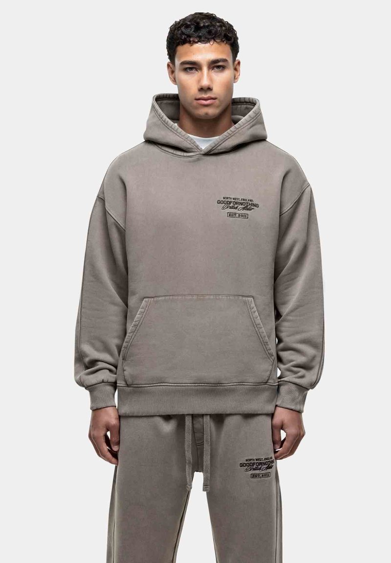 Grijze, oversized hoodie met een voorzak, een trekkoord capuchon en bedrukte tekst. Zacht materiaal en geribde manchetten maken het ontwerp af.