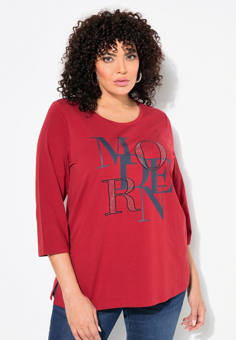 Rode longsleeve T-shirt met "MODERN" grafiek in zwart en strass-accenten. Ronde halslijn en zijsplitten aan de zoom. Zacht materiaal.