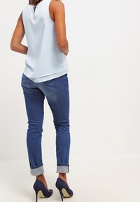 Ljusblå ärmlös blus med en nyckelhålsdetalj på ryggen, parat med mörkblå tighta jeans som är uppvikta vid fållarna och marinblå högklackade skor.