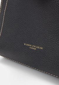 Angolo di una borsa a tracolla in pelle nera con texture, cuciture beige e logo dorato "Gianni Chiarini Firenze" impresso sulla superficie.