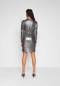 Skinande grå metallicklänning med långa puffärmar, elastisk midja och rak skärning som slutar vid mitten av låret. Kombinerad med svarta klacksandaler.