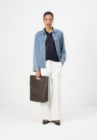 Camicia in denim, maglione blu in maglia, pantaloni bianchi a gamba larga e ballerine nere. Tiene una borsa a tracolla in pelle marrone con un manico intagliato.