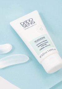 DADO SENS PURDERM normalizing cream tube next to two white cream swatches on light blue surface.