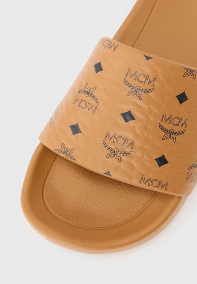 Sandale à écran tan avec semelle texturée et large bride ornée de logos MCM noirs et de motifs en forme de diamant.